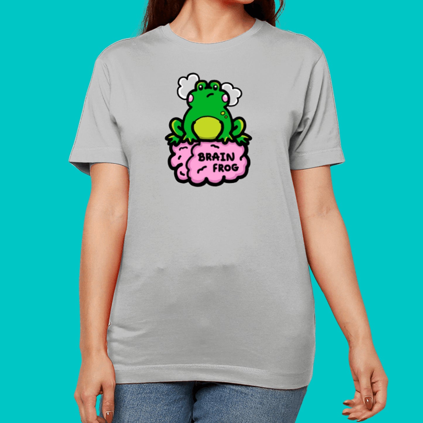 The Brain Frog T-shirt - Brain Fog in grey shown on a model posing facing forward with both hand resting by their side, photo is cropped from the chin to hips. The print is a confused frog with pink blush cheeks and two grey clouds above its head. Its sat on a pink brain with text that reads Brain Frog. The design was created to raise awareness for brain fog.
