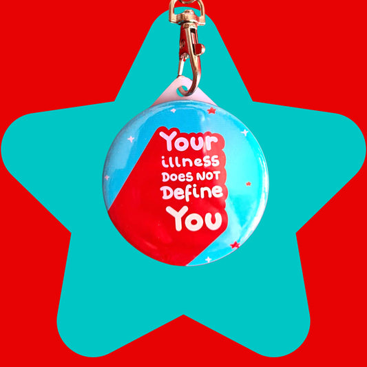 The Your Illness Does NOT Define You Keyring on a blue and red background. The silver clip blue plastic circular keyring has red and white sparkles and text reading 'your illness does not define you'. A hand drawn design raising awareness for invisible illnesses.