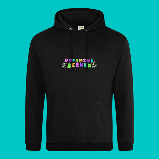 The Dopamine Seeker Black Hoodie on a blue background. The black cotton hoodie features centre rainbow bubble text that reads 'dopamine seeker' with yellow and black sparkles surrounding it. The hoodie has black drawstrings and a large centre pocket. The hoodie was designed to raise awareness for ADHD and neurodivergence.