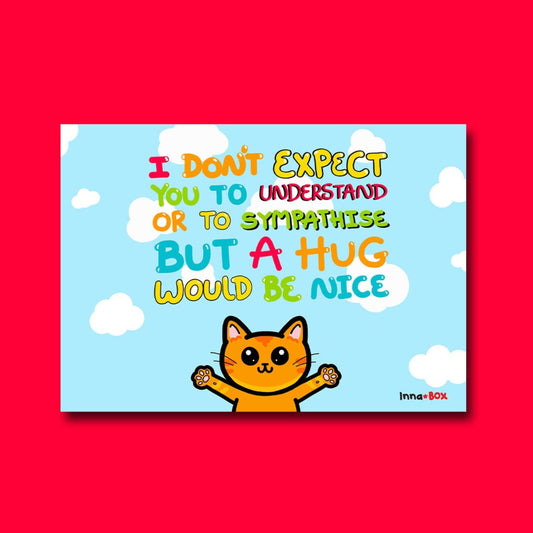 A Hug Would Be Nice - Cat Postcard shown on a red background. The light blue postcard has rainbow bubble text saying 'I don't expect you to understand or to sympathise but a hug would be nice'. Underneath the writing is an illustration of a ginger cat with big eyes and smile with it's arms wide open. The hand drawn design is made to raise awareness for invisible and chronic illnesses. 