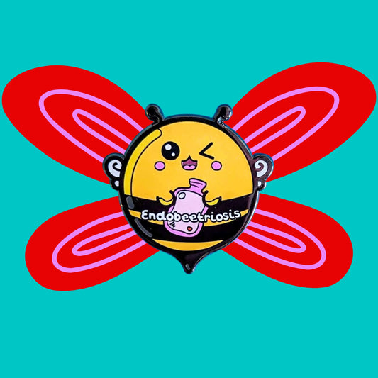 Endobeetriosis 2.0 Bee Enamel Pin - Endometriosis on a red and blue background. The enamel pin is a bumble bee with a smiley face and holding a pink hot waterbottle in its hands, across its middle is white text that reads endobeetriosis. The enamel pin is designed to raise awareness for endometriosis.