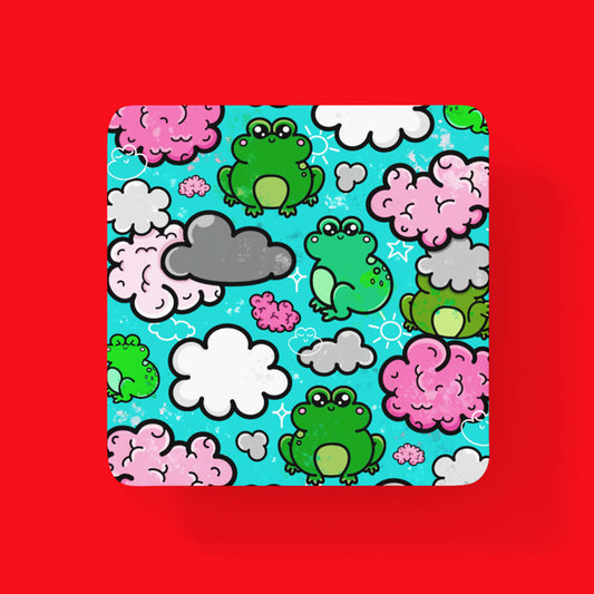 The Brain Frog Coaster - Brain Fog on a red background. The wooden coaster features various happy kawaii face green frogs with pink brain style, grey and white clouds with white sparkles on a blue background. The design was created to raise awareness for brain fog.