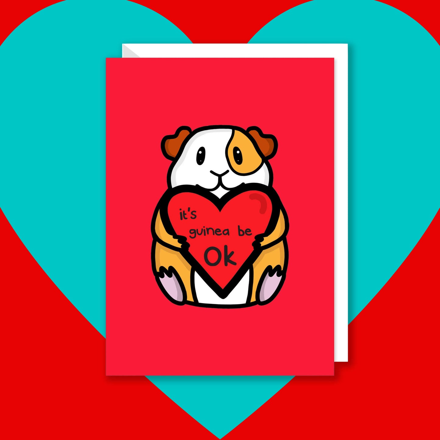 The It's Gonna Be OK Guinea Pig Card on a red and blue background with a white envelope underneath. The red a6 greeting card features a smiling orange and white guinea pig sat down holding a red heart with black text reading 'it's guinea be ok'. The hand drawn design is a perfect send a hug card as a gentle positive reminder.
