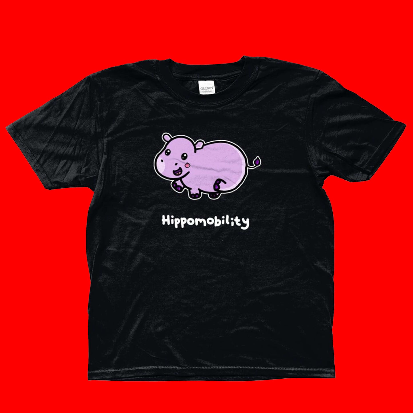 Hippomobility - Hyper Mobility Kids Tee shown on a red background. The black t-shirt has an illustration of a pink happy hippo with 'hippomobility' in white text underneath. The hand drawn design is made to raise awareness for hyper mobility.