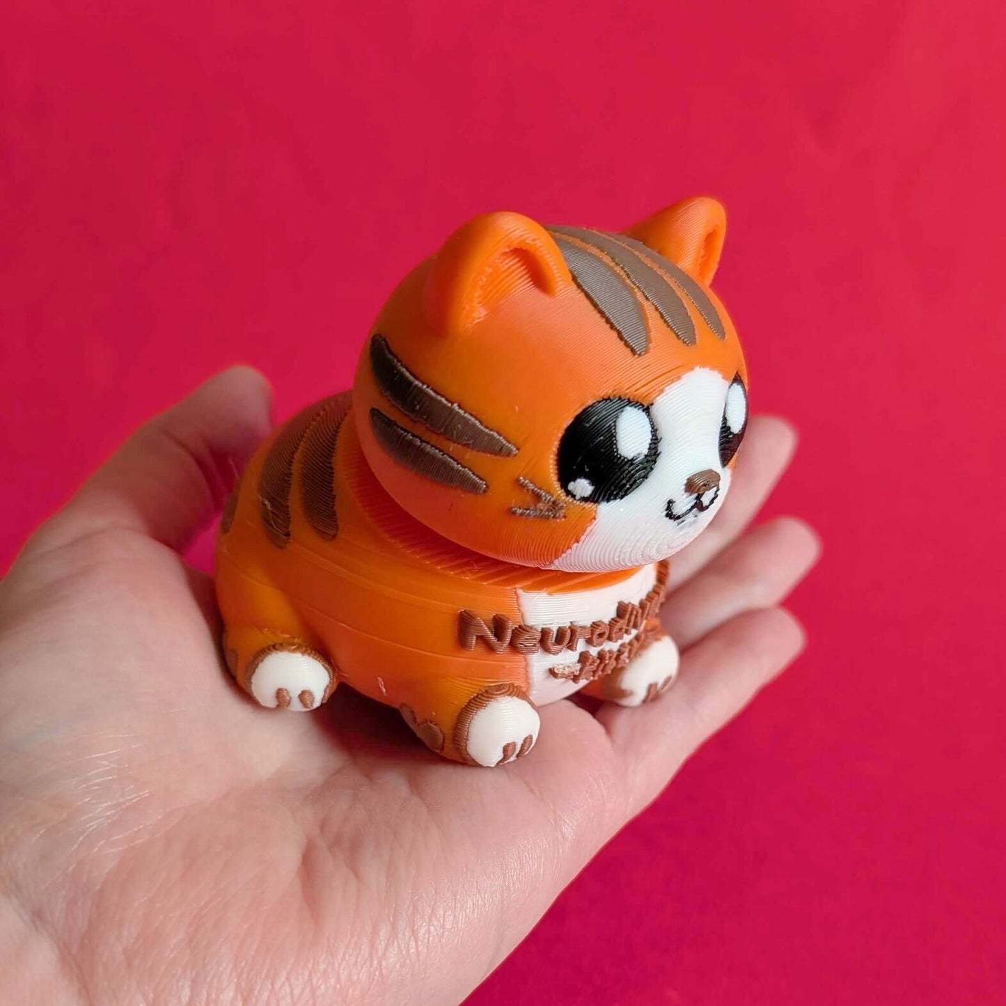 Innabox Neurodiverse Kitty Desk Buddy resting in a hand to show palm sized scale, approx 8 x 7 x 6 cm. Orange and brown 3D printed sensory fidget toy made from biodegradable polylactic acid, offering comfort and focus support for autism, anxiety, chronic illness and hidden disabilities.