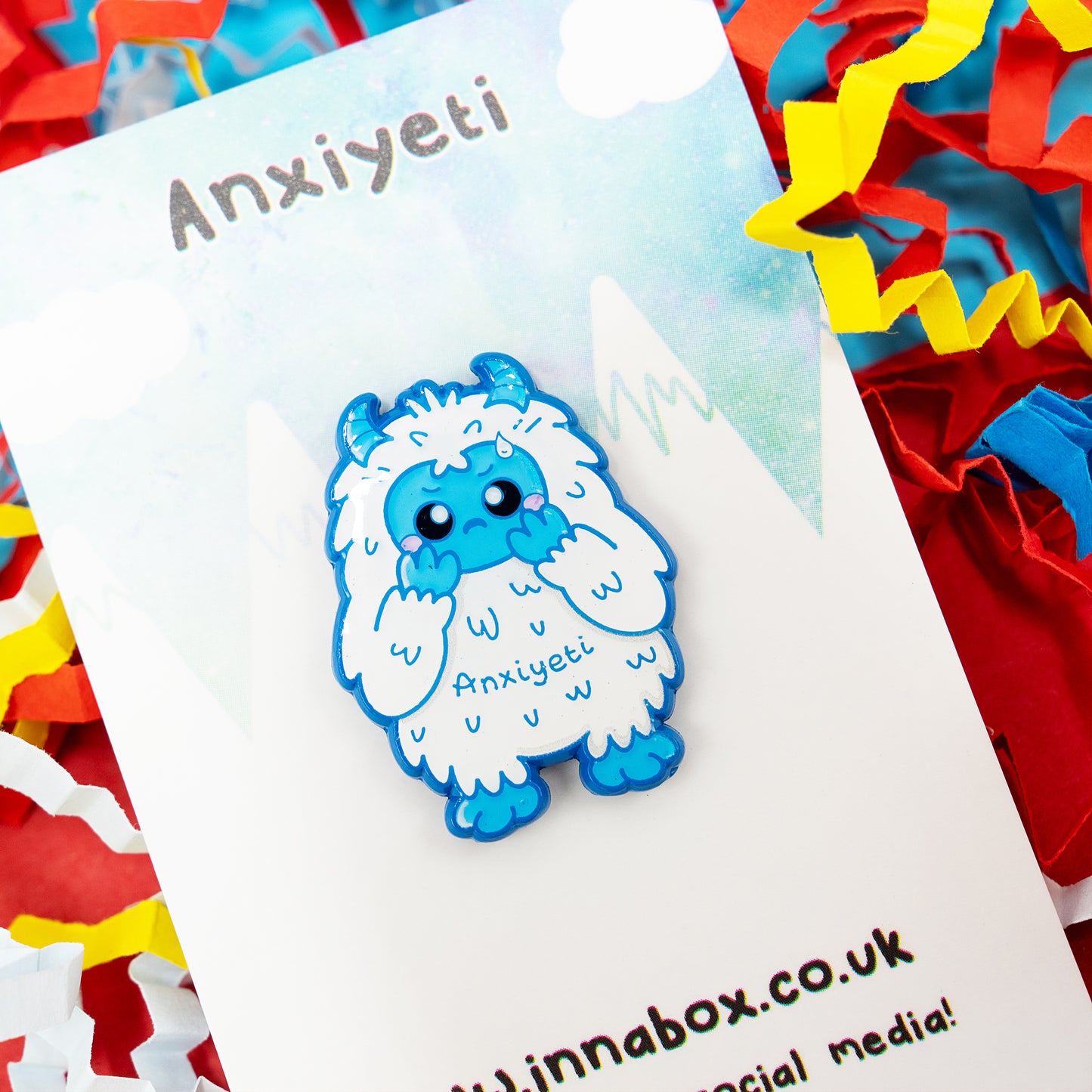 Anxi-Yeti enamel pin by Innabox featuring a cute blue and white yeti with a shy expression and the word “Anxiyeti” on its body. Displayed on a branded backing card with colourful paper confetti. Disability-inspired design spreading kindness and awareness for anxiety, chronic illness and hidden disabilities.