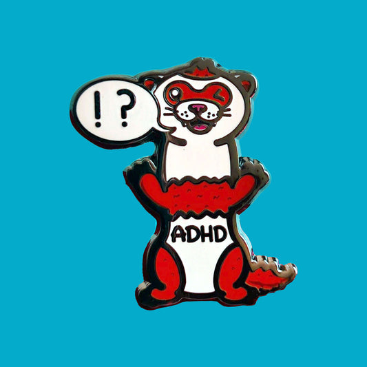 A red and white ferret enamel pin with it's mouth open in a smile and it's little teeth are showing. One of it's eyes are closed shut and it is standing on it's back legs. There is a speech-bubble from the ferret's mouth with '!?' inside it. The enamel pin is shown on a blue background. Raising awareness for ADHD - Attention deficit hyperactivity disorder.