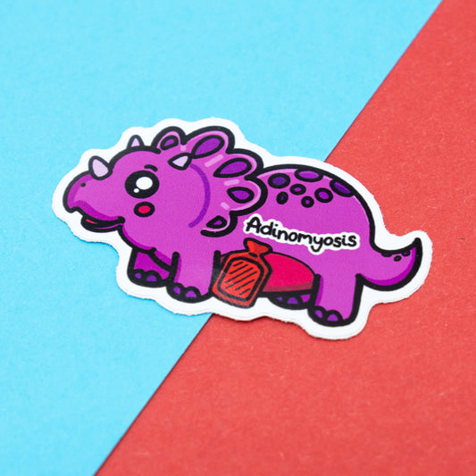 Adenomyosis awareness sticker by Innabox featuring a cute purple dinosaur with a hot water bottle and a pained expression.