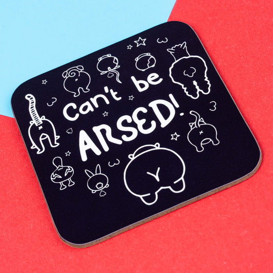 A black coaster with white hand-drawn animal butts and the phrase “Can’t be ARSED!” in playful font. Created by Innabox, this uplifting coaster is designed for those with chronic illness or hidden disabilities. Displayed on red and blue background.
