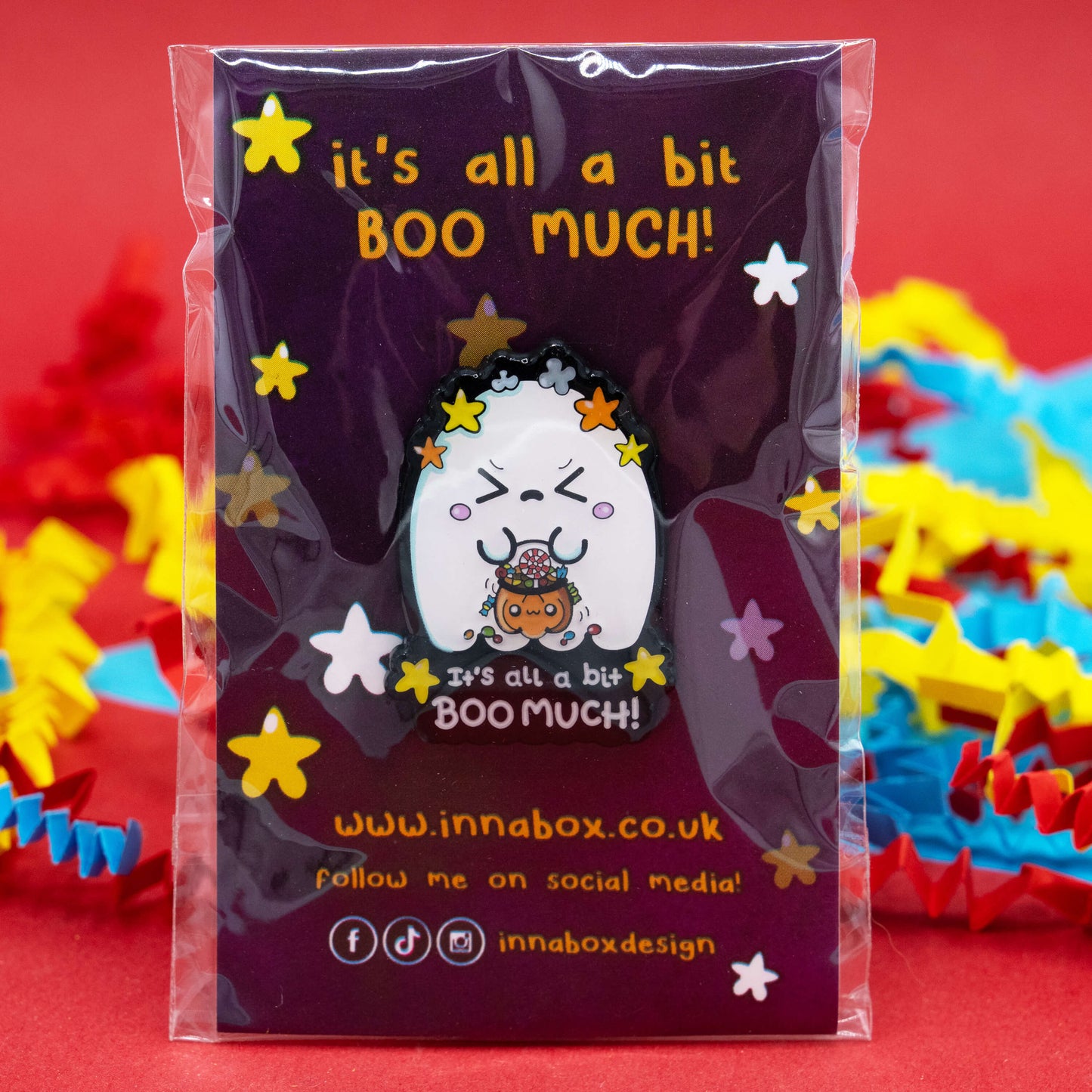 A cute Halloween ghost enamel pin by Innabox on a purple backing card reading “It’s all a bit BOO MUCH!”. The ghost holds a pumpkin bucket filled with sweets, surrounded by yellow stars. Disability-inspired design made to uplift those with hidden illnesses and neurodivergent traits.