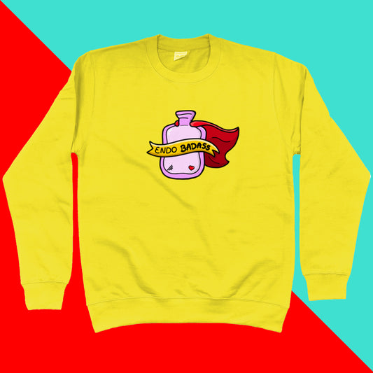 The Endo Badass Yellow Sweater - Endometriosis The sunshine yellow sweatshirt jumper has a pink hot waterbottle with a small red heart, red cape and yellow banner reading 'endo badass' in black text. The hand drawn design is raising awareness for endometriosis and pelvic pain.