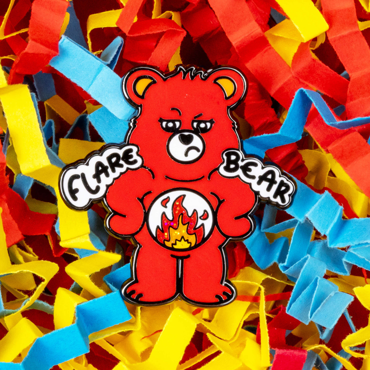 Flare Bear enamel pin shown on red, blue and yellow coloured card confetti. The enamel pin is of a red bear with a fed up expression and hands on its hips. There is a white circle on its belly with flames inside. Flare Bear is written on the pin. The enamel pin is designed to raise awareness for chronic illness flare ups.