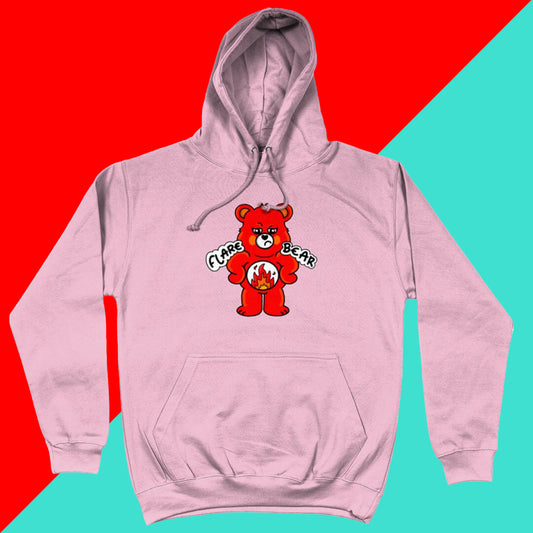Flare Bear hoodie jumper in baby pink shown on a red and blue background. The hoodie is of a red bear with a fed up expression and hands on its hips. There is a white circle on its belly with flames inside. Flare Bear is written on the hoodie. The hoodie is designed to raise awareness for chronic illness flare ups.