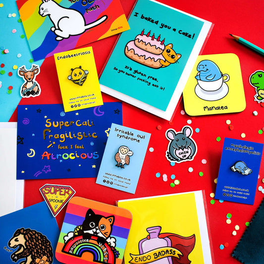 A flat lay of lots of Innabox design items including stickers, pins, coasters and card on a blue and red background with confetti