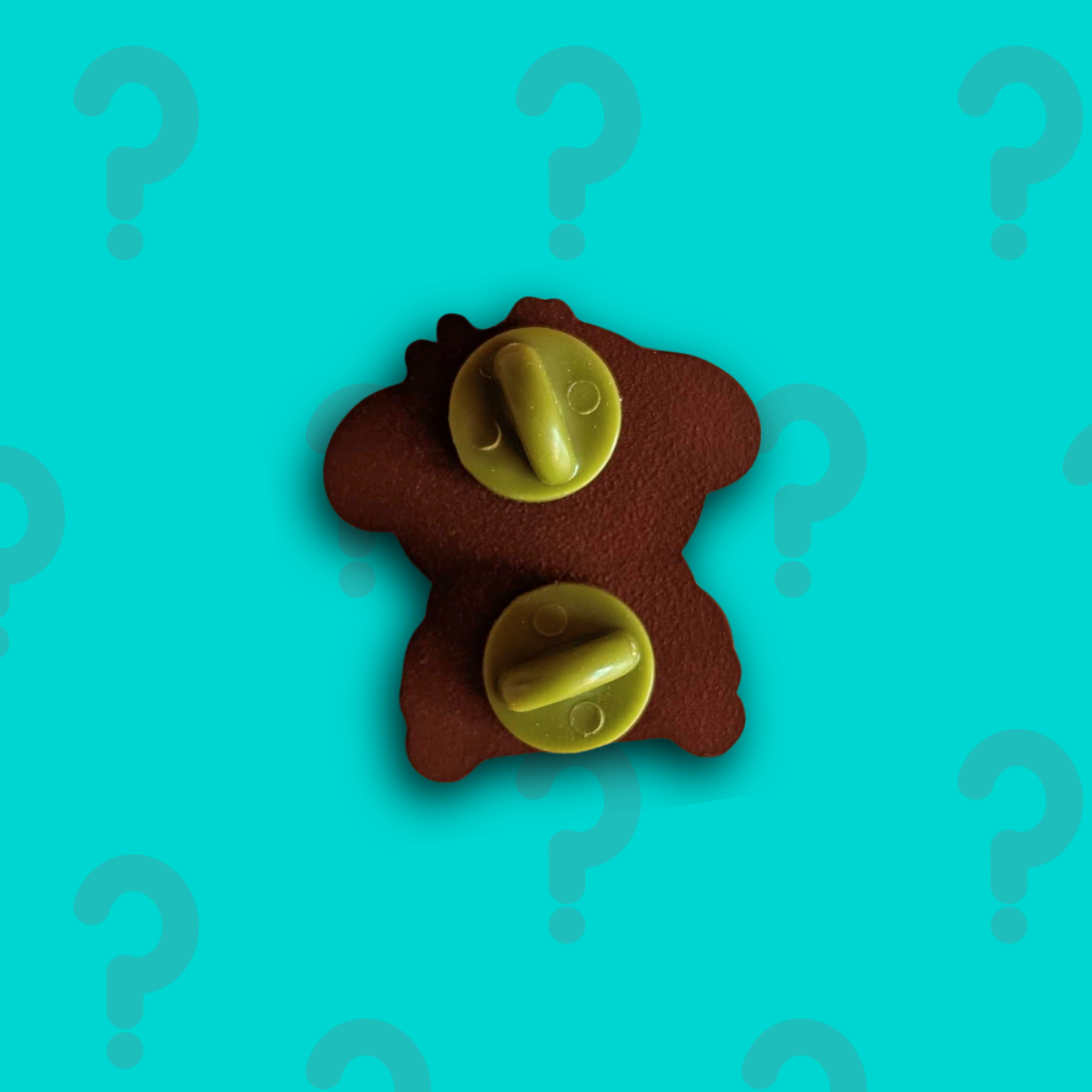 Back view of the Innabox January mystery enamel pin, showing enamel pin fastenings against a teal question mark background.