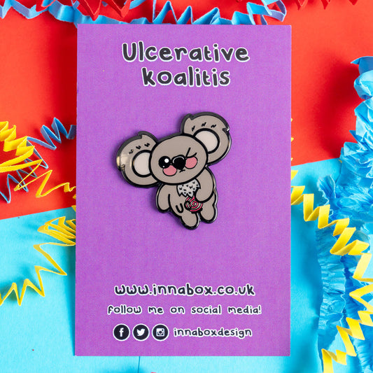 Ulcerative Koalitis Koala Enamel Pin by Innabox on a purple backing card with the text 'Ulcerative koalitis'. The card is surrounded by red, blue, and yellow paper decorations, with the brand's website and social media information displayed below.