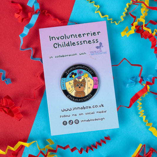 This Innabox enamel pin shows a brown terrier with a gentle, expressive face against a bright and whimsical background. The text "Involunterrier Childlessness" wraps around the top and bottom, and the pin is presented on a branded card with colourful paper streamers. Designed in collaboration with Papillon Breathwork, this pin aims to raise awareness and offer comfort to those experiencing involuntary childlessness. Perfect for those seeking support or a reminder of resilience.