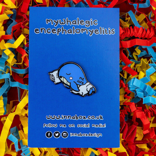 Mywhalegic Enamel Pin - Myalgic Encephalomyelitis (ME/CFS) on blue backing card on a red, blue and yellow coloured card confetti background. The enamel pin is a sleeping blue whale laying on a white pillow with a white blanket over it and ME/CFS written on its back. The enamel pin is designed to raise awareness for Myalgic encephalomyelitis or chronic fatigue syndrome
