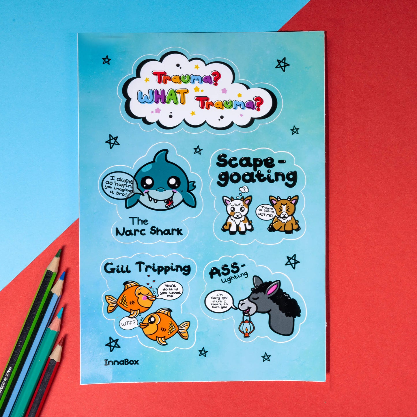 The Trauma? What Trauma? Sticker Sheet - A6 Sticker Sheet on a red and blue background with colouring pencils. The vinyl sticker sheet features 5 different designs based on types of trauma. There's a white cloud with rainbow bubble writing reading 'trauma? what trauma?', the narc shark - a smiling shark, scape-goating - two goats, Gill Tripping - two goldfish and Ass-Lighting - a donkey holding a lantern.