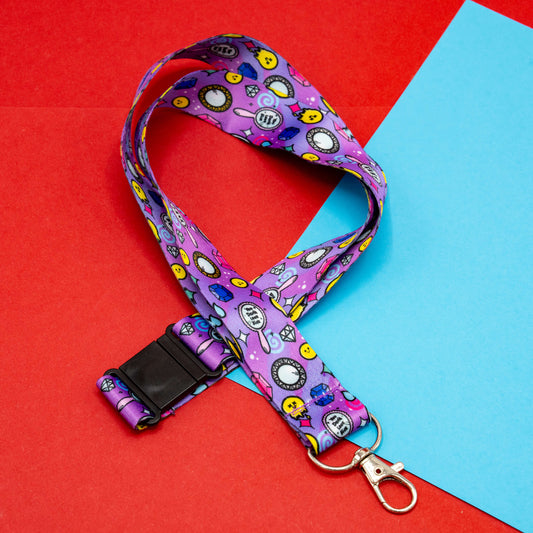 Flat lay of the “You Don’t Look Sick” lanyard by Innabox, laid out to show the full patterned strap with smiley faces, gems, and medical theme icons. Purple polyester fabric with metal dog clip and safety catch, set against a red and blue colour block background.