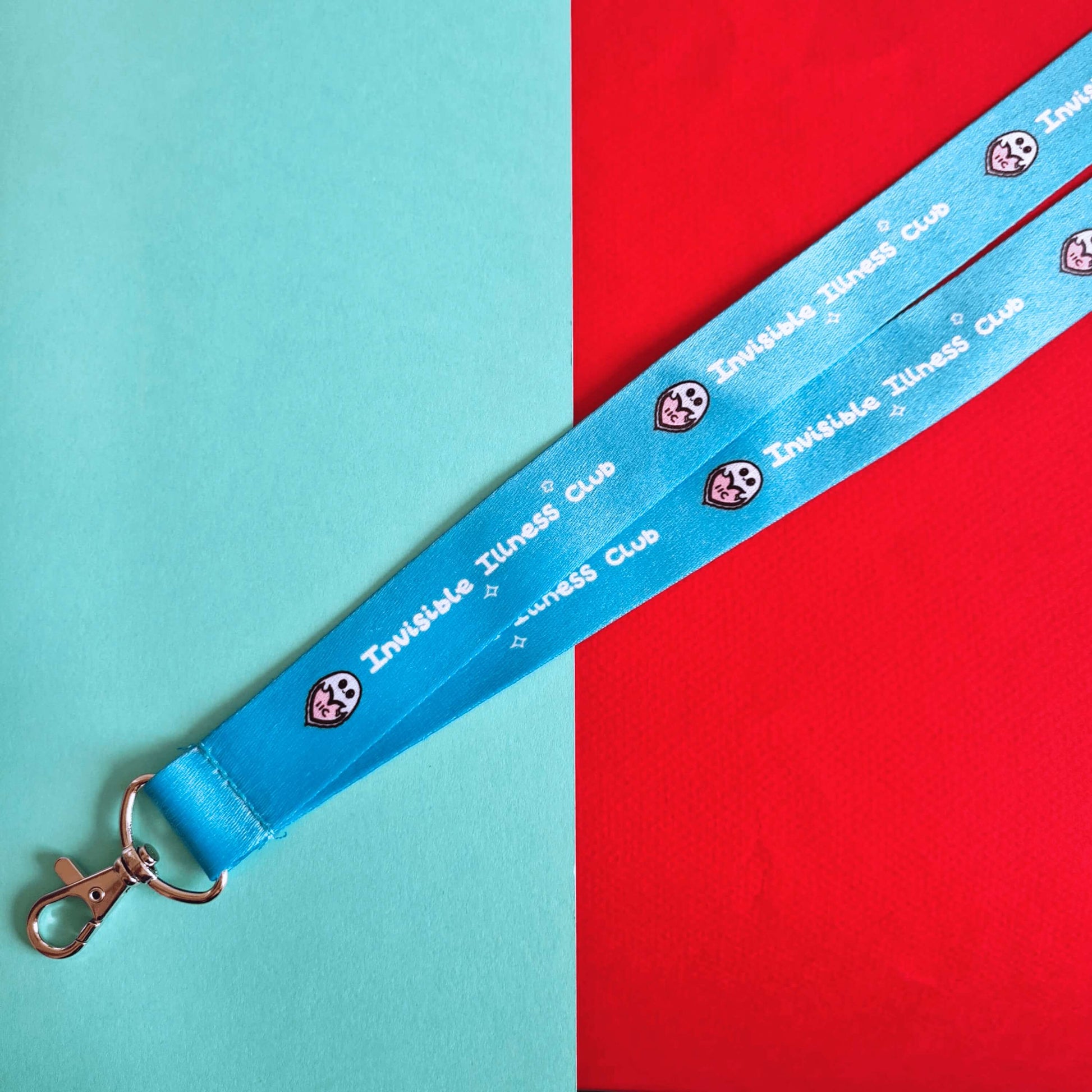 Aqua light blue lanyard with 'Invisible Illness Club' written on it in white with Innabox ghost logo and silver lobster clasp. Shown on a red and blue background. Raising awareness for invisible illnesses.