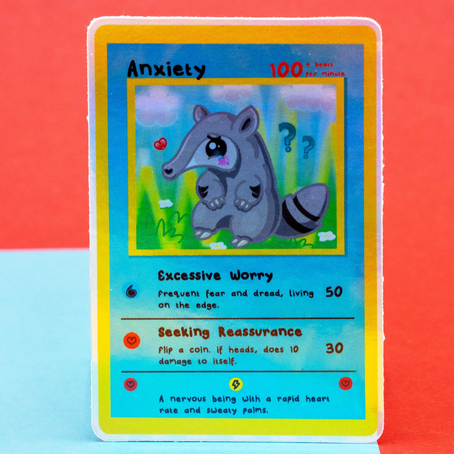 A bright product photo of the Innabox Neurodivergent Collectable Trading Card Sticker – Anxiety, featuring the anteater character with a worried expression. The colourful trading-card style design shows abilities like Excessive Worry and Seeking Reassurance. Shot against a red and blue background, ideal for fans of disability-inspired stationery.