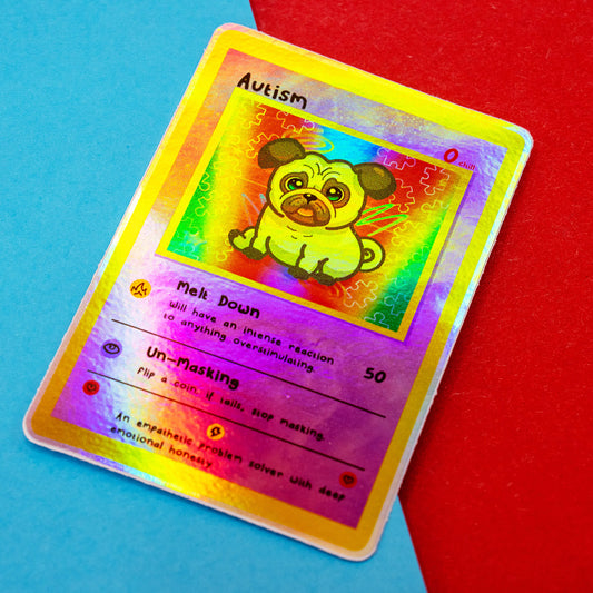 A holographic Innabox Neurodivergent Collectable Trading Card Sticker – Autism featuring a cute pug character on a rainbow puzzle-piece background. The trading-card style design includes traits like Melt Down and Un-Masking. Photographed against a blue and red backdrop, perfect for disability-inspired stationery collectors.