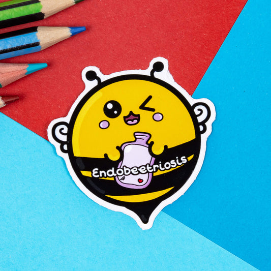 A cute round bee sticker in yellow and black holding a pink hot water bottle with Endobeetriosis written on it. It is on a blue and red background