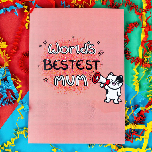 The World's Bestest Mum Cat Card on a red, blue and green background with red, yellow and blue crinkle card confetti. The pink a6 mother's day card features pink, orange and yellow dotwork background with white and black doodle text reading 'world's bestest mum'. Next to the text is a smiling black and white cat shouting through a megaphone. 