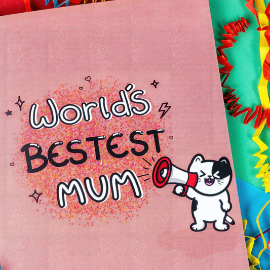 The World's Bestest Mum Cat Card on a red, blue and green background with red, yellow and blue crinkle card confetti. The pink a6 mother's day card features pink, orange and yellow dotwork background with white and black doodle text reading 'world's bestest mum'. Next to the text is a smiling black and white cat shouting through a megaphone.