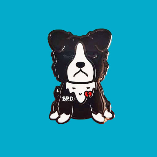 BPD Enamel Pin - Borderline Personality Disorder on a blue background. The black and white sad fluffy dog pin has a broken heart with BPD written across its chest. The pin is designed to raise awareness for Borderline Personality Disorder.