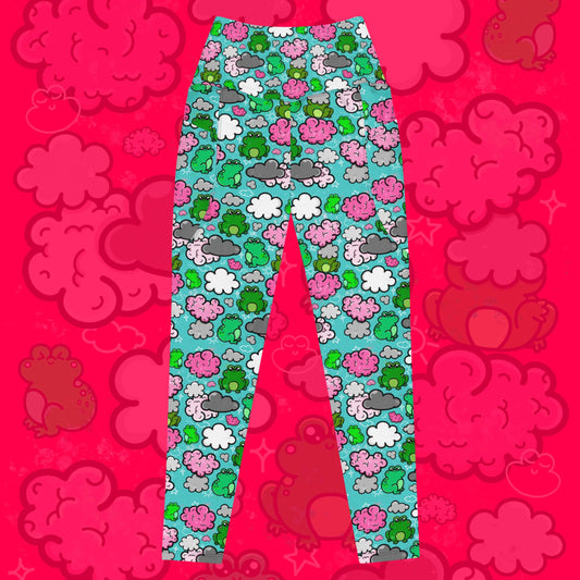 The Brain Frog Leggings with pockets - Brain Fog on a red background with a faded brain frog print. The leggings are an aqua blue base with various green kawaii face frogs with pink blush cheeks, pink brain style clouds, white and grey clouds and white sparkles all over. The design was created to raise awareness of Brain Fog.