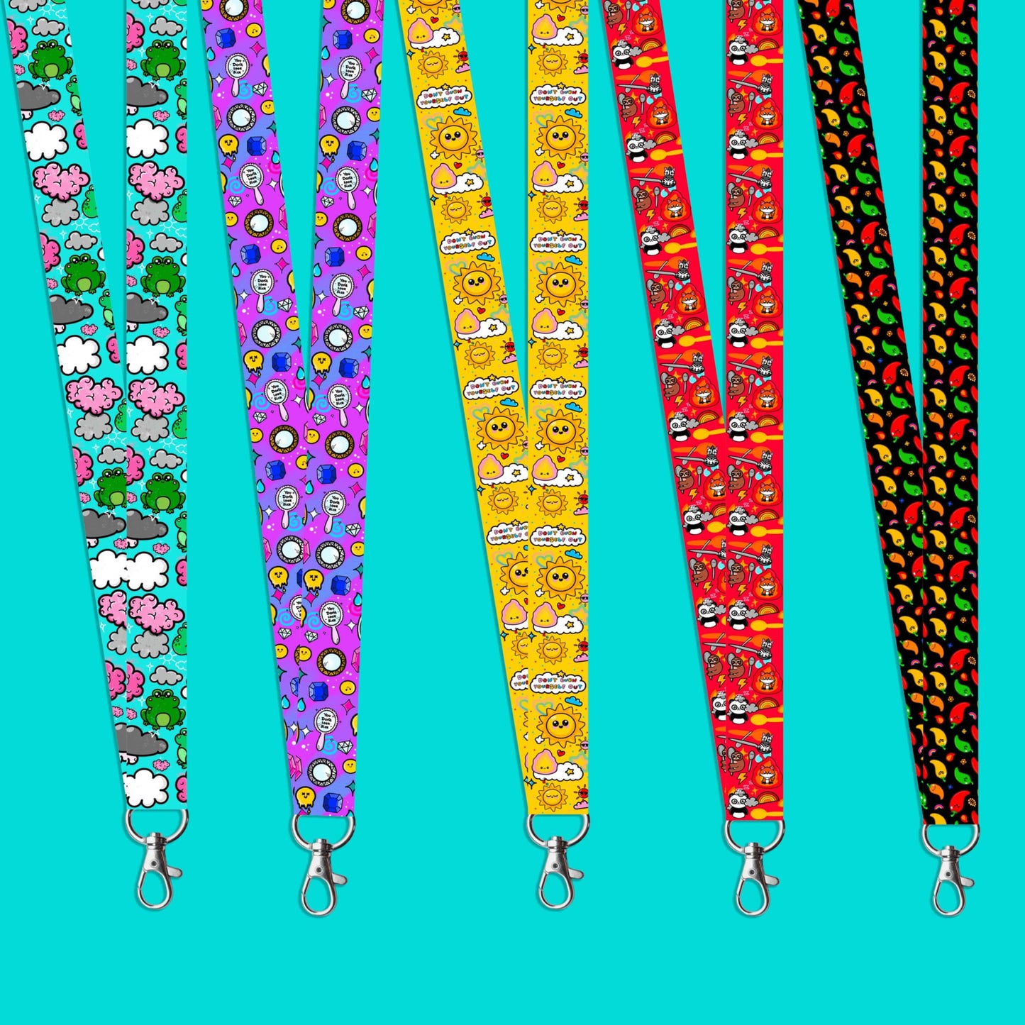 The Don't Burn Yourself Out Lanyard on a blue background with various other innabox lanyards. The lanyard is yellow with various kawaii face sunshines, sparkles, hearts, pink flames and pink, blue and white clouds with don't burn yourself out inside in rainbow. Design inspired by the self care movement.