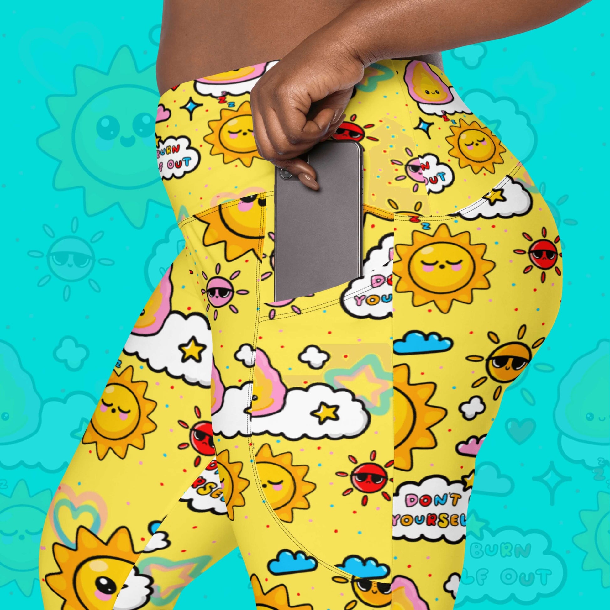 Close up of the Don't Burn Yourself Out Leggings with pockets on a model over an aqua blue background with a faded don't burn yourself print overlayed. The model is putting a silver phone in the side pocket. The print is yellow with various kawaii face sunshines, sparkles, hearts, pink flames and pink, blue and white clouds with don't burn yourself out inside in rainbow. Design inspired by the self care movement.