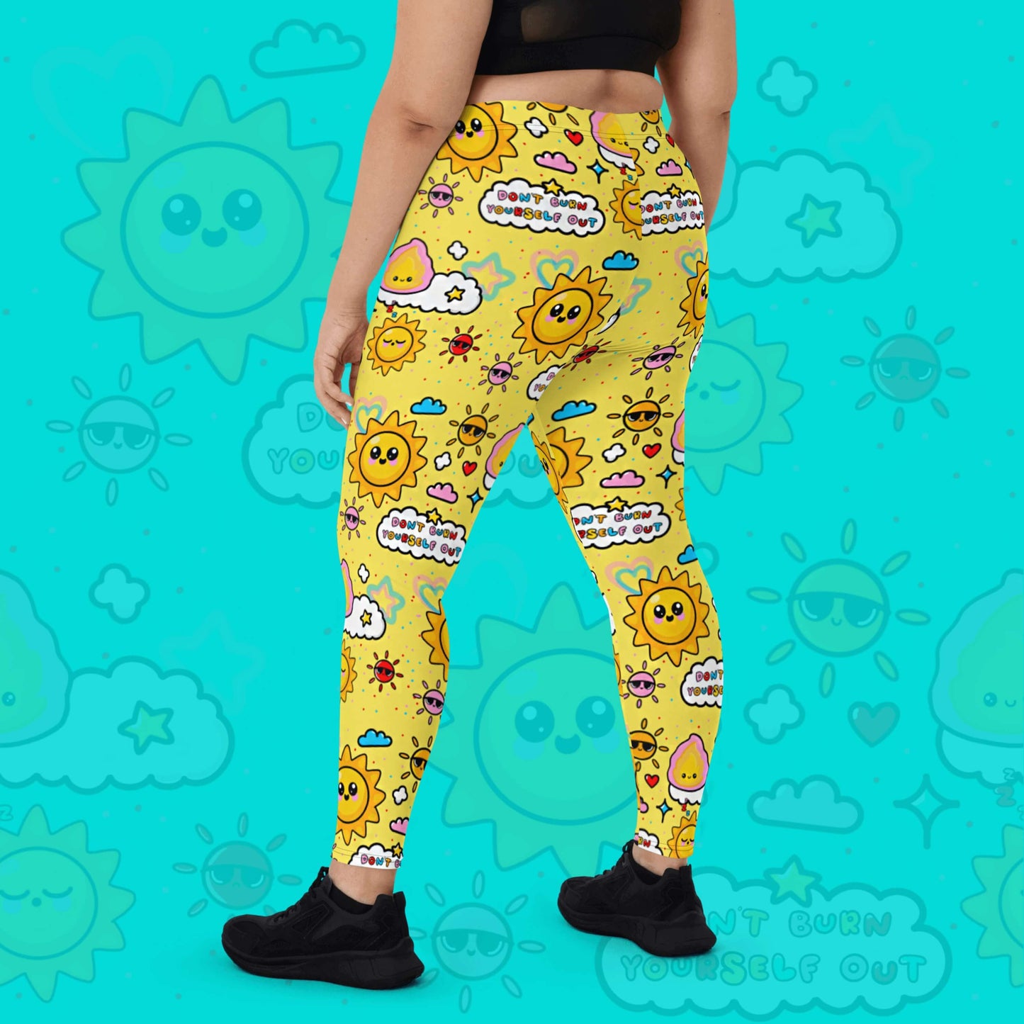 The Don't Burn Yourself Out Leggings on a model over an aqua blue background with a faded don't burn yourself print overlayed. The model is facing away with their left leg bent and both hands resting by their side. The print is yellow with various kawaii face sunshines, sparkles, hearts, pink flames and pink, blue and white clouds with don't burn yourself out inside in rainbow. Design inspired by the self care movement.