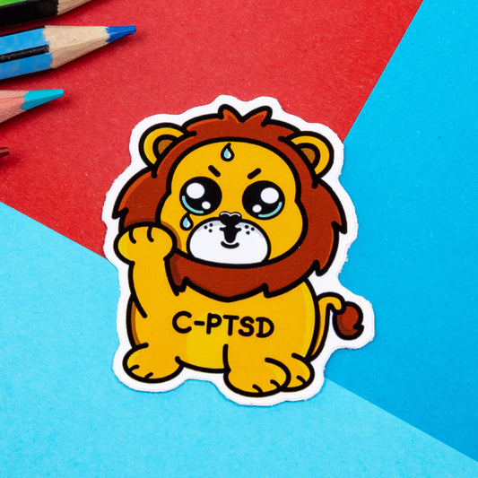 A red and blue graphic background with a yellow crying smiling and sweating male lion with its paw raised in the middle. Across the lions chest is C-PTSD. The sticker design is raising awareness for complex post traumatic stress disorder.