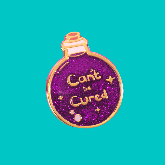 The Can't Be Cured Potion Bottle Enamel Pin on a blue background. A gold outlined circular potion bottle with a glittery purple middle with two pastel pink bubbles, gold sparkles and gold text that reads 'can't be cured'. The design was inspired by chronic illnesses.