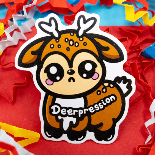 A close-up of the Innabox Deerpression 2.0 sticker featuring an adorable sad deer character with soft brown fur, heart-shaped antlers, and the word “Deerpression” written on its body. Surrounded by colourful shredded paper on a red and blue background, this gloss vinyl sticker promotes gentle awareness of mental health and is made to uplift people with invisible disabilities or chronic illness.