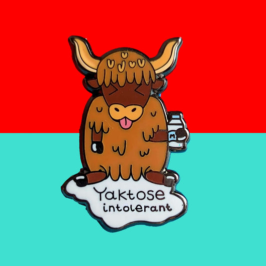 Yaktose Intolerant Enamel Pin - Lactose Intolerant on a blue and red background. The enamel pin is a yak sat holding a bottle of milk with it's tongue out looking disgusted. There is a puddle of milk under the yak with black text that reads 'yaktose intolerant'. The hand drawn design is made to raise awareness for lactose intolerance 