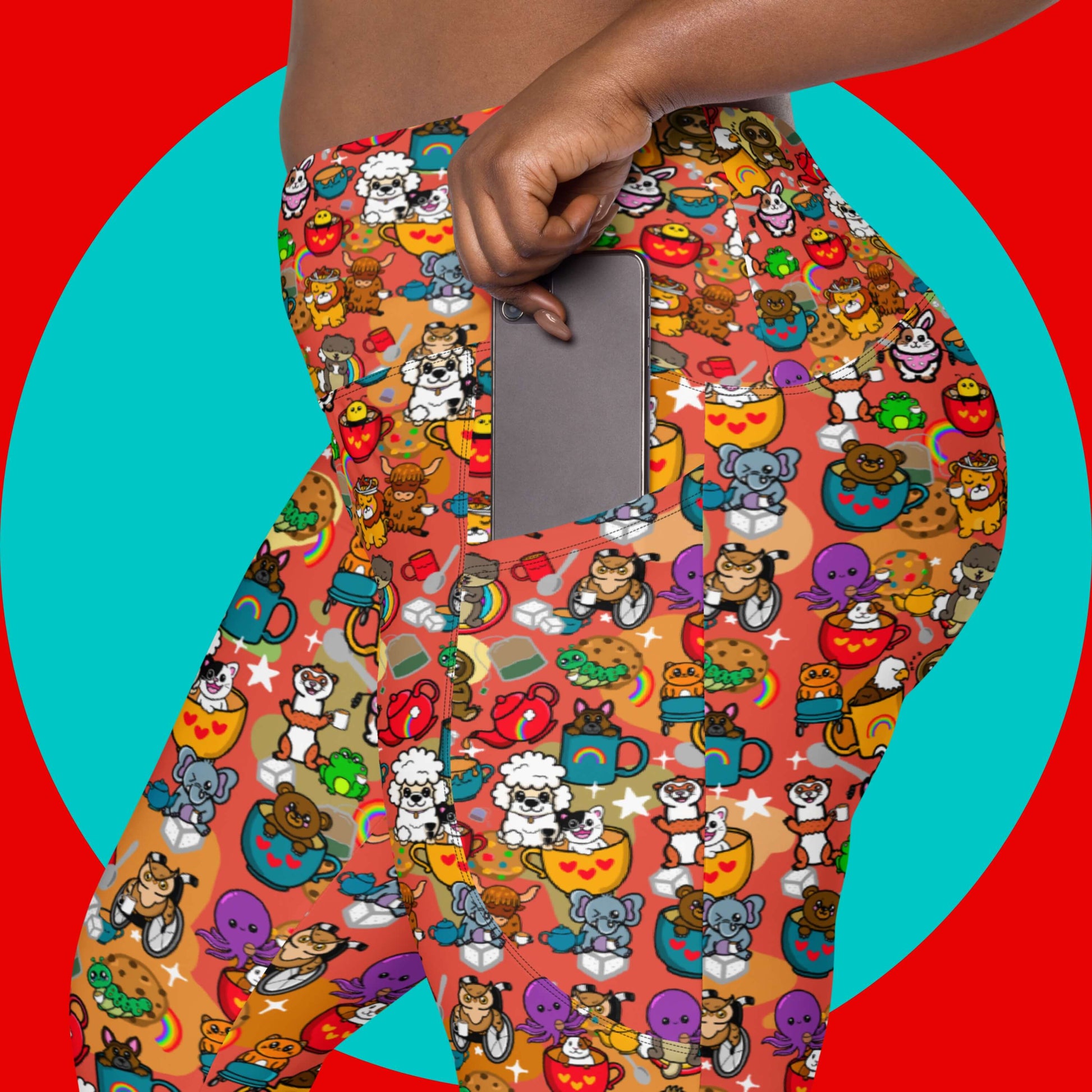 Close up of the Disabili Tea and Biscuits - Disability Leggings with pockets being modelled by a femme person tucking a silver phone into the side pocket on a red and blue background. The leggings feature various disabled and chronically ill animal characters drinking tea, sitting in tea mugs and holding up mugs. There is also various cookie biscuits, tea bags, sugar cubes, teapots, rainbows, sparkles and tea spills all underneath. The leggings are a punny gift raising awareness for disabilities.