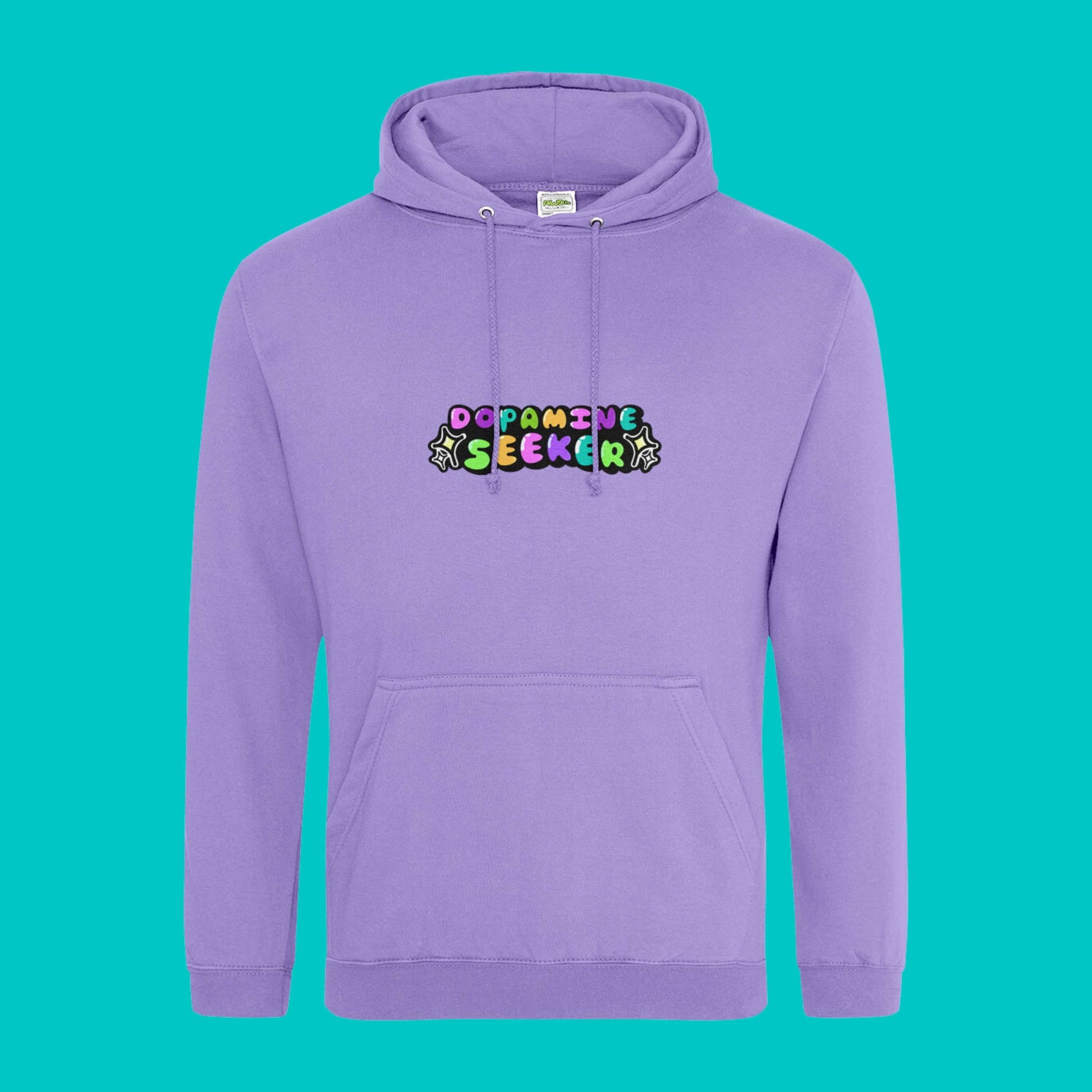 The Dopamine Seeker Hoodie in digital lavender on a blue background. The hoodie design has 'dopamine seeker' written in the middle in rainbow bubble font and black sparkle outlines. The hoodie has pastel purple drawstrings and a large centre pocket. Design is raising awareness for ADHD and neurodivergence.