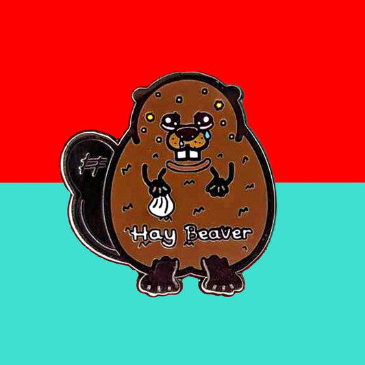 Hay Beaver Enamel Pin - Hay Fever on a red and blue background. The enamel pin is a brown beaver with watery eyes, dripping nose and yellow spots on face and is holding a tissue with it's little hand. Hay beaver is written across its belly. The enamel pin is designed to raise awareness for hay fever or allergic rhinitis