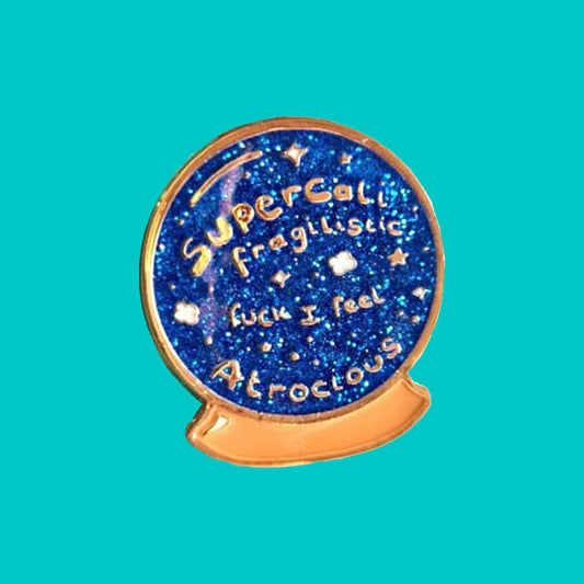 I Feel Atrocious Enamel Pin - Blue circle enamel pin with the words supercali fragilistic fuck I feel atrocious' on. It is on a green, red and blue background with pencils in in the corner of the shot. Enamel pin designed to raise awareness for invisible illnesses
