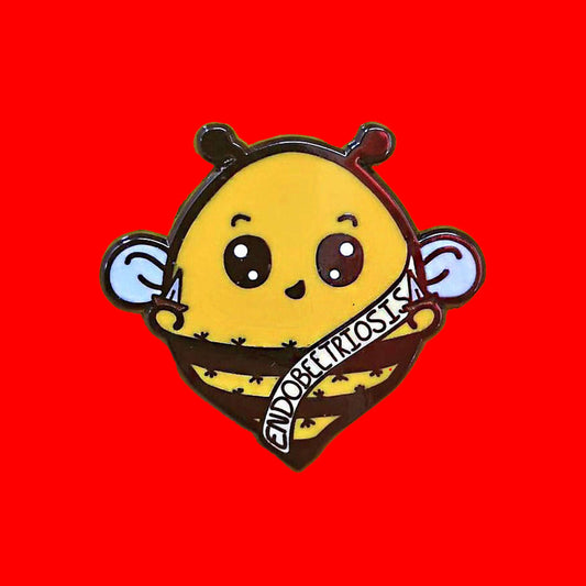 Endobeetriosis Enamel Pin - Endometriosis on a red background. The enamel pin is a bumble bee with a smiley face and holding little daggers in its hands. The bee is wearing a white sash that has endobeetriosis written accross it. The enamel pin is designed to raise awareness for endometriosis