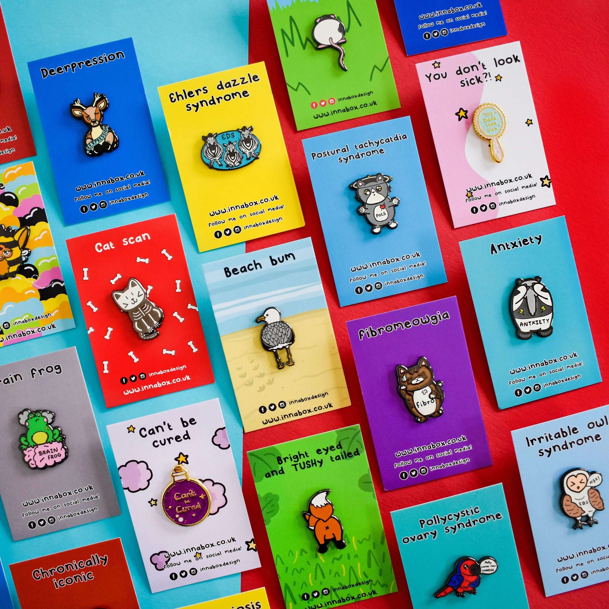an array on Innabox enamel pins on backing card shown on a red and blue background. The enamel pins are designed to raise awareness for chronic illnesses