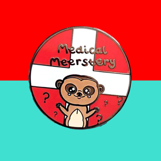 Medical Mystery Meerkat Enamel Pin on a red and blue background. The enamel pin is a red circle with white first aid cross and a cute meerkat at the bottom with big eyes and has it's little arms open wide. There are black question marks around the meerkat and 'medical meerstery' written above it in black writing. Hand drawn design made to raise awareness for invisible and chronic illnesses