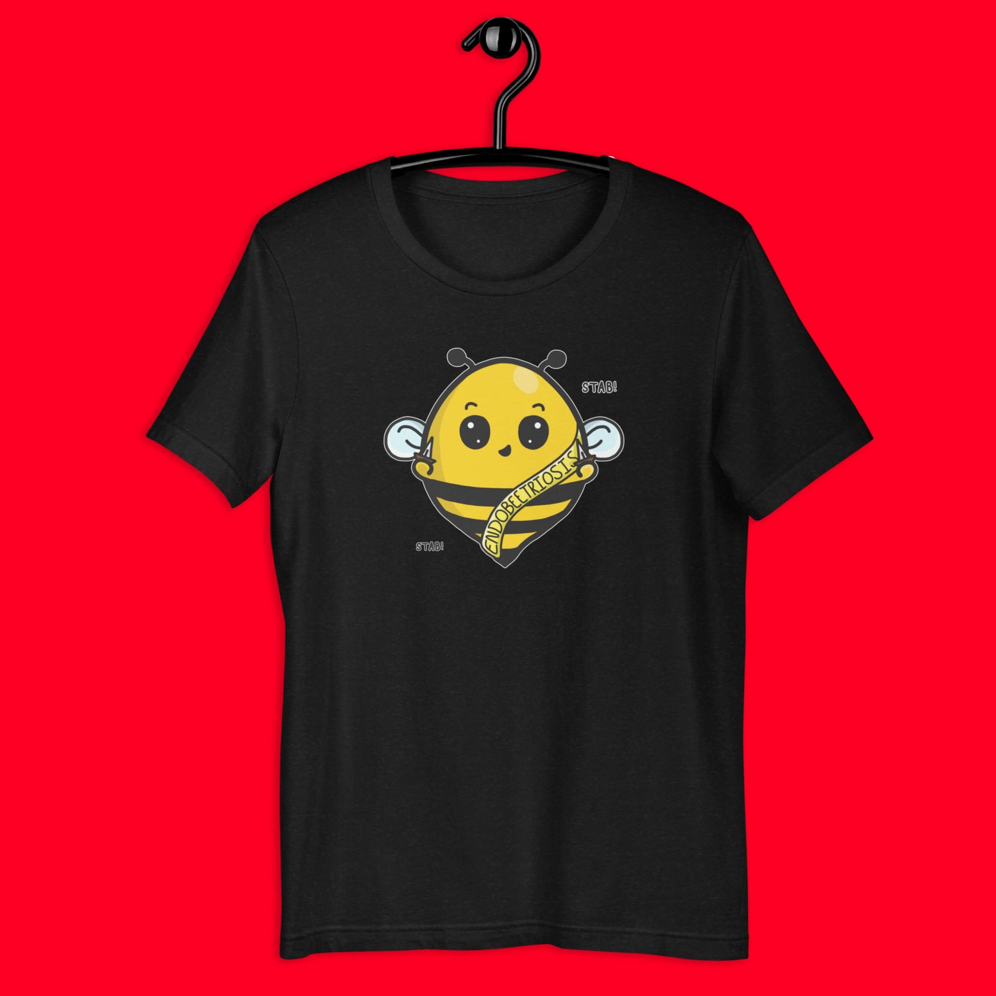 The Endobeetriosis Tee - Endometriosis hung on a black hanger over a red background. The black short sleeve tshirt features a smiling happy bumblebee holding small daggers with a yellow banner reading 'endobeetriosis' with the words 'stab! stab!' surrounding the buzzy bee. The hand drawn design is raising awareness for endometriosis. 