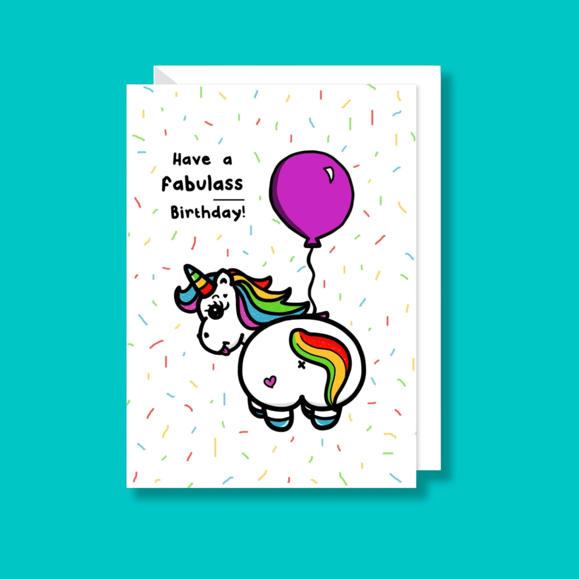 a white greeting card with an illustration of a unicorn with it's bum to the camera and looking back over it's shoulder with it's tongue out. The unicorn has rainbow coloured hair and horn and a pink love heart on it's bum and is holding a pink balloon. There is rainbow confetti all over the card and 'Have a fabulass Birthday!' is written in black with 'ass' underlined. The sassy birthday card is on a blue background with a white envelope underneath.