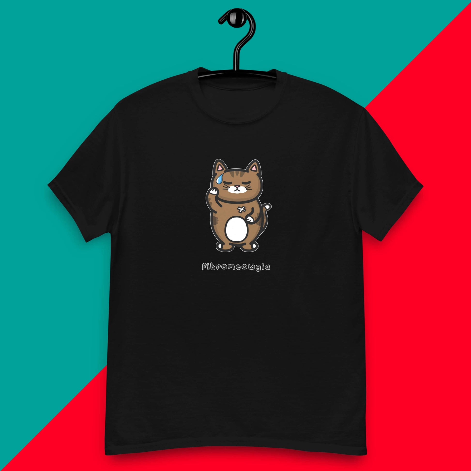 The Fibromeowgia Cat Tee - Fibromyalgia Syndrome hanging on a black hanger over a red and blue background. The black short sleeve tshirt features a sad brown tabby cat with a sweat droplet clutching its body with a white bandaid and bottom text reading 'fibromeowgia'. The hand drawn design is raising awareness for fibro fibromyalgia syndrome.