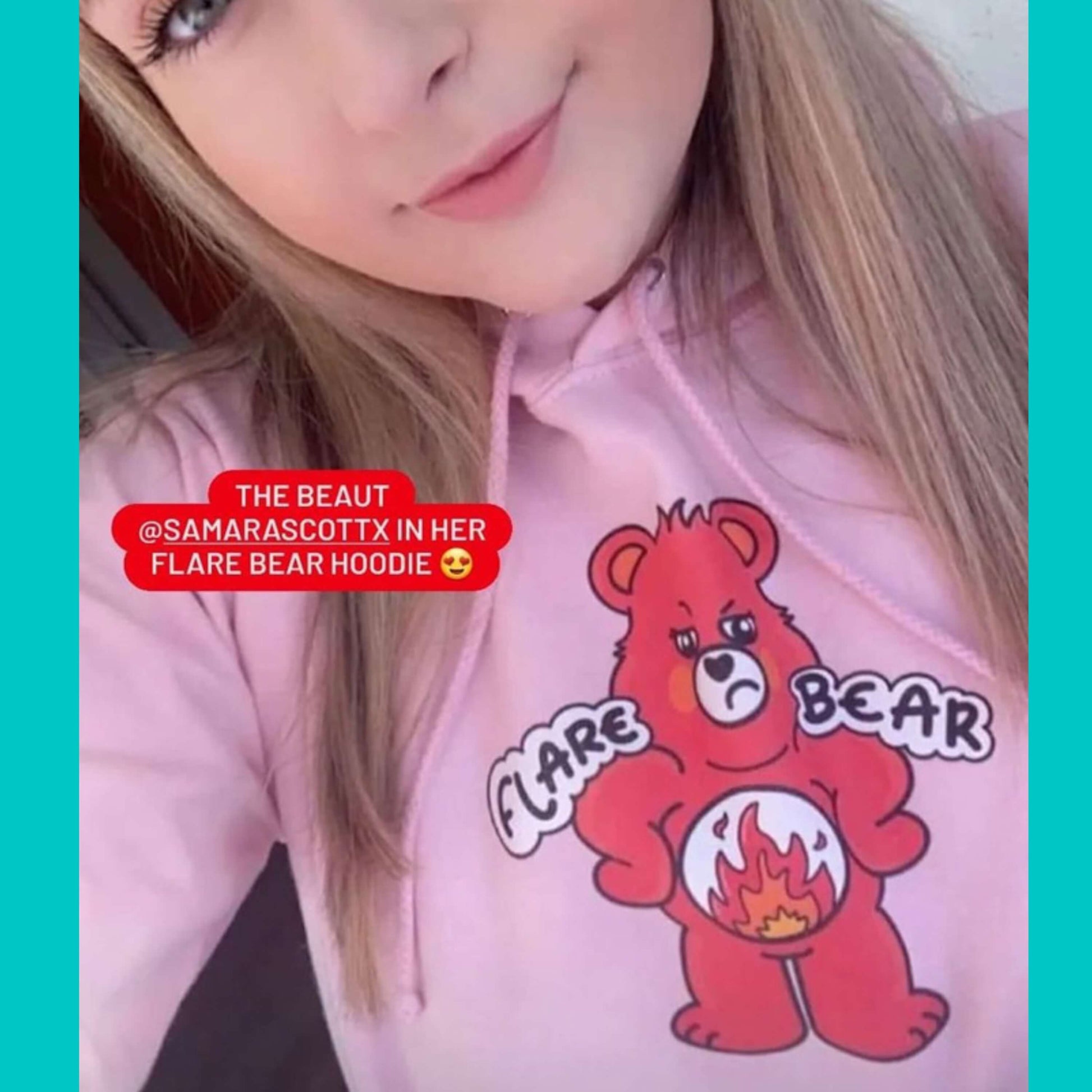 Flare Bear hoodie jumper in baby pink modelled by a blonde femme smiling innabox customer. The hoodie is of a red bear with a fed up expression and hands on its hips. There is a white circle on its belly with flames inside. Flare Bear is written on the hoodie. The hoodie is designed to raise awareness for chronic illness flare ups.